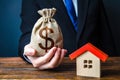 Man holds out a money bag near the house. Bank approval for issuing a mortgage loan. Favorable terms and conditions, low interest