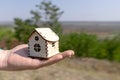 Man holds out a small wooden house in the palm of his hand. Wooden house in the palm of your hand, against the backdrop