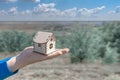 Man holds out a small wooden house in the palm of his hand. Wooden house in the palm of your hand, against the backdrop