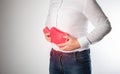 A man holds a red heating pad with hot water near his abdomen. Removal of spasms and pains in the abdomen, thermotherapy. Relieve