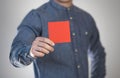 A man holds a red square sheet of paper. A flyer in the hands of a man. Prepared for your text. Isolated on a gray background