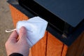 Man holds a respirator in his hand and is about to throw it in the trash in the park. he picked up the respirator on the ground to