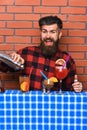 Man holds shaker on brick wall background. Barman with beard and happy face makes cocktail. Barman or hipster makes