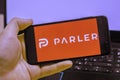 A man holds a smartphone with the logo of the social network parler laptop in the background in a blur Royalty Free Stock Photo