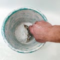 Man holds spatula against the background of old plastic bucket. Process of manual mixing construction putty.