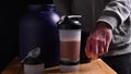 A man holds sports supplements in his hands. Sheker with a cocktail, packaging with whey protein on the table. Fitness