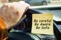 A man holds on to the steering wheel, next to a sticker with the inscription - Be careful. Be aware. Be safe.