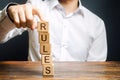 A man holds a tower of blocks with the word Rules from falling. Setting clear rule and restrictions. Leadership and discipline