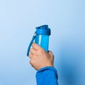 A man holds a water bottle high in his hand on a blue background. Sport drink concept. Copy space for your text Royalty Free Stock Photo