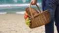 A man holds a wicker basket with food and wine for picnic on the beach. Summertime relaxation and recreation concept Royalty Free Stock Photo