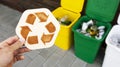 Man holds the wooden recycle sign in hand in front of three dustbins