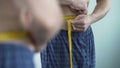 Man in home clothes measuring volume of his hips after debilitating diet