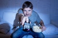 Man at home lying on couch at living room watching tv eating popcorn bowl using remote control