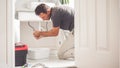 Man At Home Mopping Up Water From Leaking Pipe in Bathroom