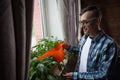 Man at home office watering plants. Smiling freelancer taing care of flowers at window. Break during working process