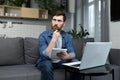 The man at home is studying remotely, uses a laptop, sitting at home on the couch, recording a lecture Royalty Free Stock Photo