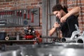 Man in home workshop garage work drilling metal with drill, repair iron pipe on the workbench full of wrenches, diy and craft