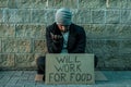 A man, homeless, a man asks for alms on the street with a sign will work for food. Concept of homeless person, addict, poverty,
