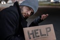 A man, homeless, a person asks for alms on the street with a Help sign. Concept of homeless person, addict, poverty, despair