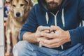 Man with a hood and a dog uses the smartphone