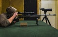 A man in a hood reload and shoots with a sniper rifle at a shooting range
