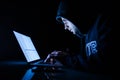 Man in a hood working in front of a laptop hacker cracking programs in the night