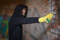 A man draws graffiti on a brick wall with a canopy covering his face