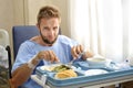 Man in hospital room eating healthy diet clinic food in upset moody face expression Royalty Free Stock Photo