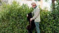 Man hugging his black dog next to a bush full of leaves Royalty Free Stock Photo