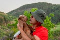 Man hugs brown baby goat with rural background