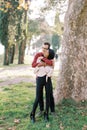 Man hugs woman from behind by the shoulders at the plane tree and looks away Royalty Free Stock Photo