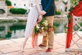 Man hugs woman with a bouquet of flowers in her hands while standing on the pier near a decorative screen against the