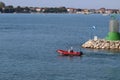 A man in an inflatable motorboat, swims past a stone breakwater with a dangerous signal beacon. Rest on the water in paradise.