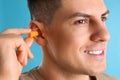 Man inserting foam ear plug on light blue background, closeup Royalty Free Stock Photo