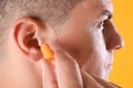 Man inserting foam ear plug on yellow background, closeup Royalty Free Stock Photo