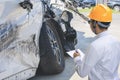 Man inspector checking writing on clipboard in garage of dealership With car crash Wait for mechanic In warranty period car