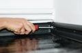 A man is installing a black plastic skirting board to a white wallpapered wall