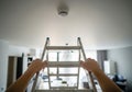 Man installing or checking smoke detector on ceiling from a ladder at home. Home safety and fire protection concept Royalty Free Stock Photo