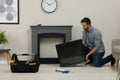 Man installing electric fireplace near wall in room