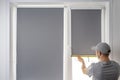 Man installing gray roller blinds on window