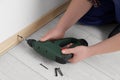Man installing plinth on laminated floor with screwdriver in room, closeup Royalty Free Stock Photo