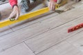Man installing rectangular shaped floor tiles in kitchen. Applying adhesive before installation and verifying afterwards