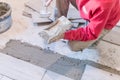 Man installing rectangular shaped floor tiles in kitchen. Applying adhesive before installation and verifying afterwards