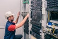 A man installs new equipment in a modern data center. An engineer in a white helmet mounts a stack of switches in a rack. The Royalty Free Stock Photo