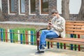 A man in the isolation mode walks on the street and crouches on a bench, looks at the phone screen Royalty Free Stock Photo