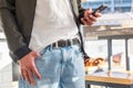 Man in jacket and jeans is standing indoors and using cellphone. Close up of hands and phone. Concept of online Royalty Free Stock Photo