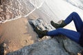 Man in jeans and green boots with laces sits and relaxes overlooking the sea in fine weather