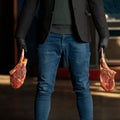 Man in jeans holds t-bone steaks. Butcher holding two large pieces of raw meat on bone. Blurred background. Close-up Royalty Free Stock Photo