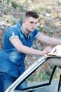 Man in jeans, leaning on an old damaged car