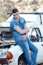 Man in jeans, sitting on an old damaged car